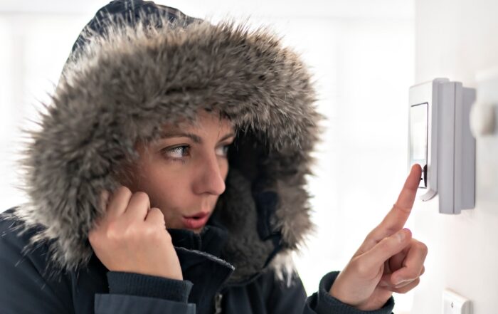woman adjusting home hvac thermostat while wearing black hooded jacket with fur brim