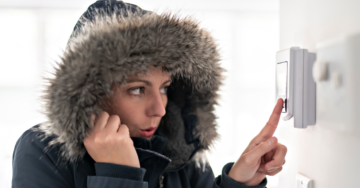 woman adjusting home hvac thermostat while wearing black hooded jacket with fur brim